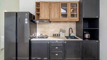 Eine kompakte Küche mit schwarzen Schränken, einem Edelstahl-Kühlschrank, einem Gasherd und einem eingebauten Backofen.