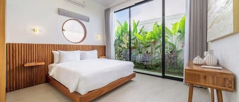 Un dormitorio moderno con una cama de madera, un espejo redondo y vistas a la vegetación a través de un ventanal grande.