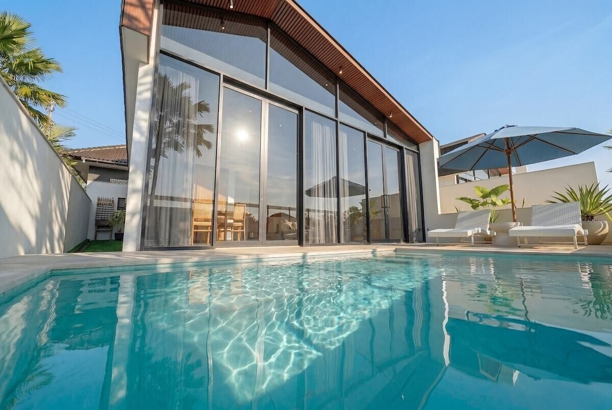 Une maison moderne dotée d’une piscine, de grandes fenêtres et d’un espace salon extérieur.