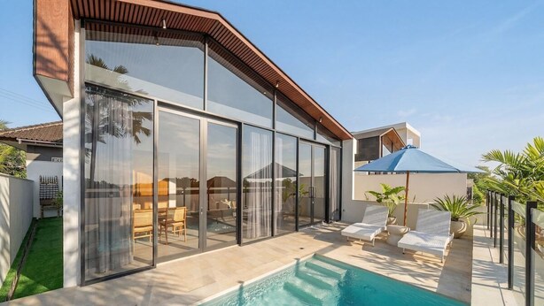 Una casa moderna con piscina, amplios ventanales y mobiliario de exterior.