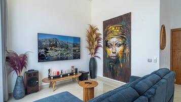 Un salon comprenant un canapé, une table basse, un tableau, un haut-parleur et un vase contenant des plantes séchées.