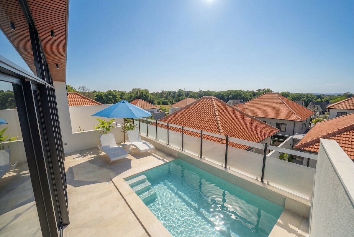 Ein Dachpool mit freiem Blick auf angrenzende Häuser, einem blauen Sonnenschirm und einem weißen Zaun.