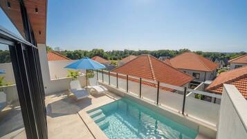 Ein Dachpool mit freiem Blick auf angrenzende Häuser, einem blauen Sonnenschirm und einem weißen Zaun.