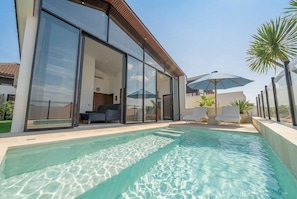 A modern house with a swimming pool, large glass doors, and outdoor seating. - Modern 3BR near Pandawa Beach w Private Pool&Patio (Badung Regency)