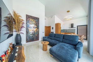 A modern living room with a blue sofa, a wooden coffee table, and a painting on the wall. - Modern 3BR near Pandawa Beach w Private Pool&Patio (Badung Regency)
