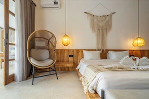 Une chambre d’hôtel avec un lit, une chaise en osier, deux lampes suspendues, une décoration murale en macramé et une vue par la fenêtre.
