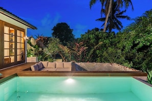 A swimming pool with a wooden deck, surrounded by lush greenery and a palm tree. - Hidden 3BR Oasis in Serene Ubud w Huge Pool+Patio (Gianyar Regency)