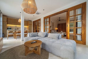Ein modernes Wohnzimmer mit einem großzügigen Ecksofa, einem Holztisch und einem Essbereich, im Hintergrund befindet sich eine Küche.