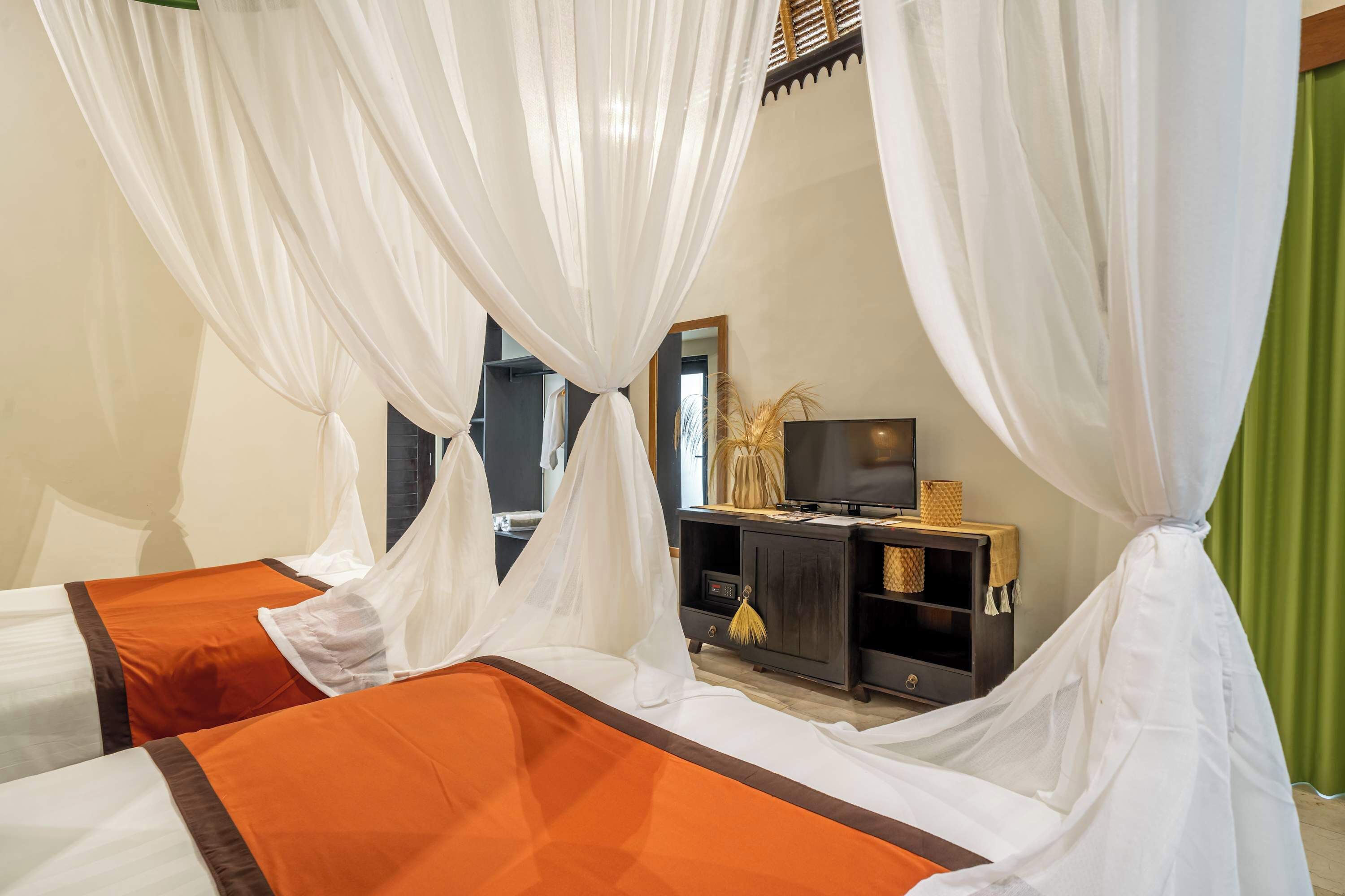 A hotel room with a bed, a television on a wooden cabinet, and a green curtain.