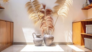 A room with a tiled floor, a wooden cabinet, a metal vase with dried plants, and a metal pitcher. - Boho 2BR w Pool+Patio+Garden in Peaceful Ubud (Gianyar Regency)