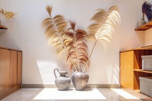 Ein Zimmer mit Fliesenboden, einem Holzschrank, einer Metallvase mit Trockenpflanzen und einem Metallgießer.
