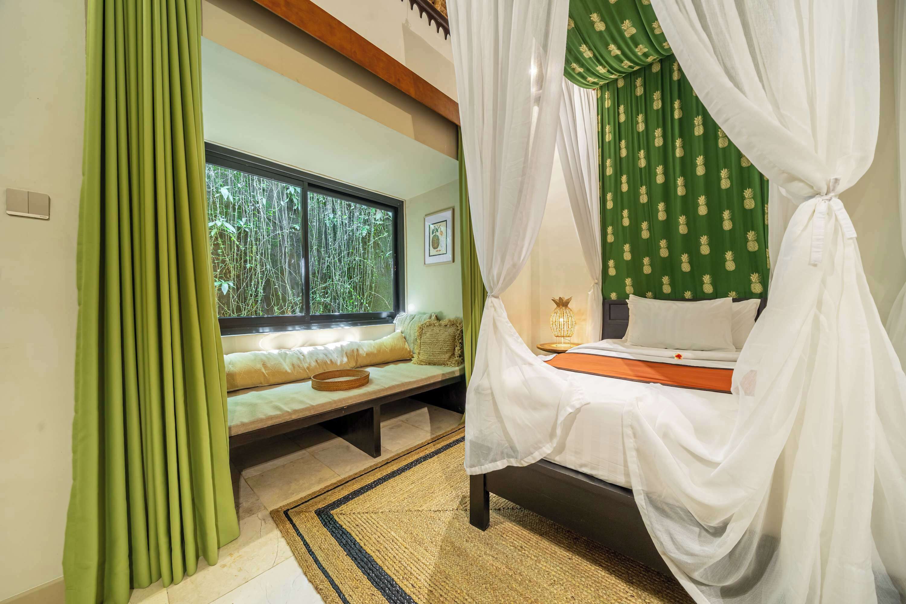 A room with a bed, a window with a view of greenery, a bedside lamp, and a curtain.