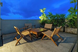 A rooftop terrace with a wooden table and chairs, surrounded by potted plants.