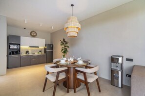 A modern kitchen with grey cabinets, a round dining table with white chairs, and a hanging light fixture. - Grey Stones - Designer 2BR Villa w Rooftop, Pool & Beach Nearby (Badung Regency)