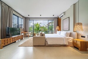 Ein modernes Schlafzimmer mit einem großen Bett, einem Fernseher, einem Schreibtisch und Blick auf Grünflächen.