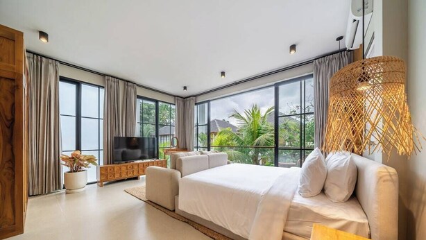 A modern bedroom with a large bed, a TV, and a view of greenery outside. - Cozy 3BR in Ubud w Bathtubs, Ricefield Views, Pool (Tegallalang)