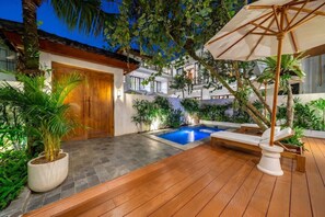 Uma área de piscina com deck de madeira, uma espreguiçadeira e uma porta de madeira.