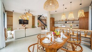 A modern dining area with a wooden table set for four, surrounded by wicker chairs. - Cozy 3BR in Ubud w Bathtubs, Ricefield Views, Pool (Tegallalang)