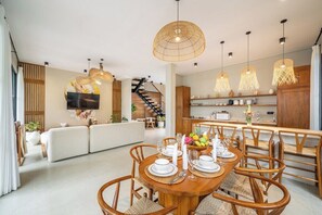 Uma sala de jantar moderna com uma mesa de madeira posta para quatro pessoas, rodeada por cadeiras de vime.