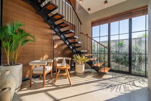 Ein modernes Interieur mit einer Holztreppe, großen Fenstern und Zimmerpflanzen.