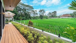 A wooden deck with a view of a rice field and a traditional building in the distance. - Luxe 3BR Gem in Tropical Ubud w Pool, Patio&Garden (Gianyar Regency)