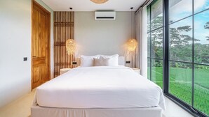 A bedroom with a large bed, two bedside lamps, a ceiling light, and a view of greenery through a large window. - Luxe 3BR Gem in Tropical Ubud w Pool, Patio&Garden (Gianyar Regency)