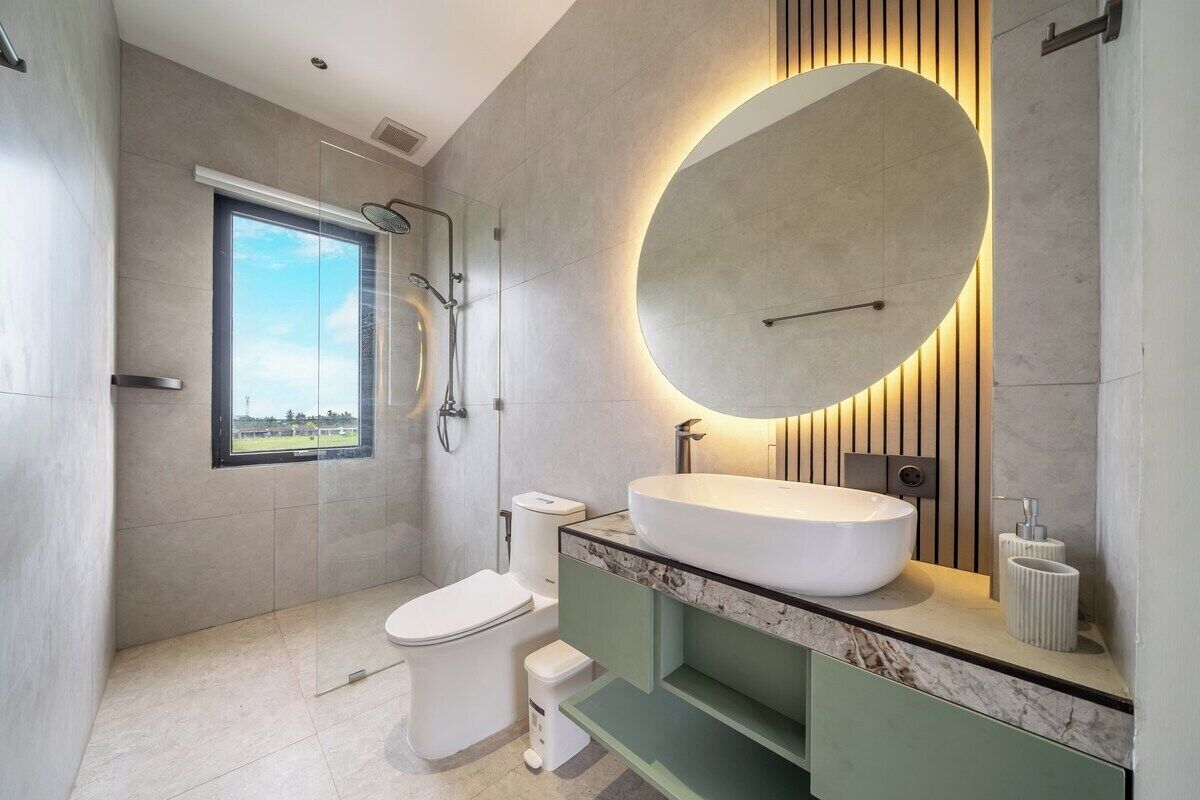 A modern bathroom with a large oval mirror, a freestanding bathtub, and a toilet.
