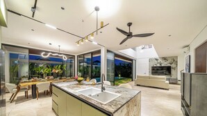 A modern kitchen with a marble countertop, a built-in sink, and a dining area with a wooden table and chairs. - Luxe Jungle 4BR in the Heart of Ubud w Pool, Patio (Gianyar Regency)