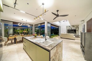 A modern kitchen with a marble countertop, a built-in sink, and a dining area with a wooden table and chairs. - Luxe Jungle 4BR in the Heart of Ubud w Pool, Patio (Gianyar Regency)