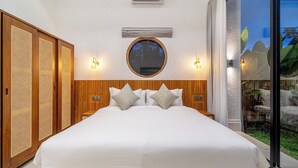 Un dormitorio con una cama grande, cabecera de madera, dos luces fijadas a la pared, un espejo redondo y una puerta corrediza de vidrio que da a un espacio al aire libre.