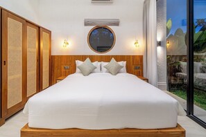 Ein Schlafzimmer mit einem großen Bett, einem Holzkopfende, zwei Wandleuchten, einem runden Spiegel und einer Schiebetür aus Glas zu einem Außenbereich.