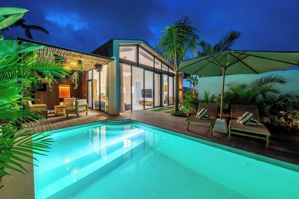 Une maison moderne dotée d’une piscine, d’un espace salon extérieur et de plantes tropicales.