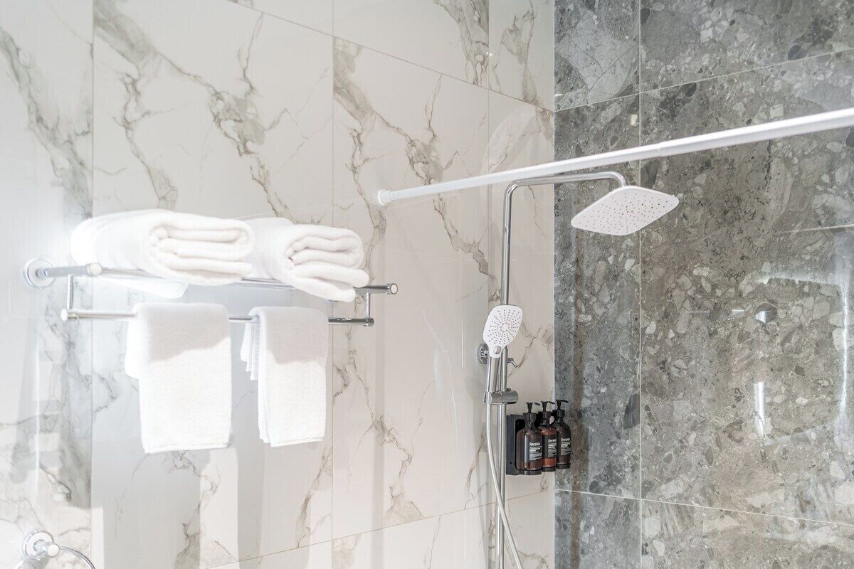 Ein Badezimmer mit Marmorwänden, einem Handtuchhalter mit gefalteten Handtüchern, einem Duschkopf und einer Shampoo-Flasche.