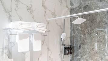 Ein Badezimmer mit Marmorwänden, einem Handtuchhalter mit gefalteten Handtüchern, einem Duschkopf und einer Shampoo-Flasche.