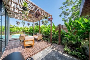 Une terrasse en bois avec des meubles d’extérieur, une piscine et une végétation luxuriante.