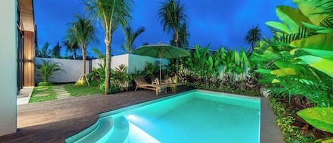 Una piscina con cubierta de madera, rodeada de plantas tropicales y palmeras.