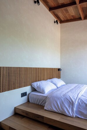 A bedroom with a wooden headboard, a bed with white bedding, and a wooden bench at the foot of the bed. - ART1 - Designer Villa with 2 Bedrooms & Pool, Ubud (Gianyar Regency)