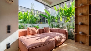 A modern living room with a sectional sofa, a wooden floor, and a large window overlooking a garden. - ART1 - Designer Villa with 2 Bedrooms & Pool, Ubud (Gianyar Regency)