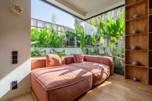 A modern living room with a sectional sofa, a wooden floor, and a large window overlooking a garden. - ART1 - Designer Villa with 2 Bedrooms & Pool, Ubud (Gianyar Regency)