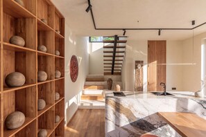 A modern interior with a wooden shelving unit holding spherical objects, a marble countertop with a sink, and a staircase leading to an upper level. - ART1 - Designer Villa with 2 Bedrooms & Pool, Ubud (Gianyar Regency)
