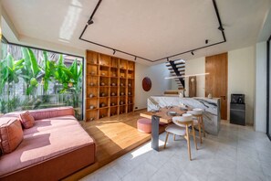 A modern interior with a sofa, dining area, kitchen, and a large window with plants. - ART1 - Designer Villa with 2 Bedrooms & Pool, Ubud (Gianyar Regency)