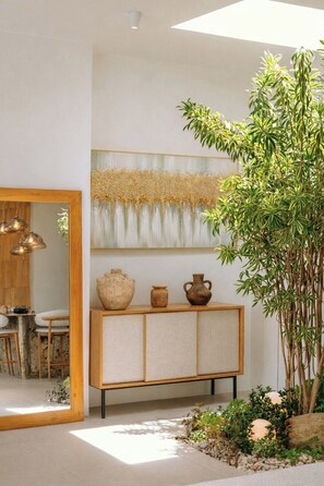 Ein modernes Interieur mit einem Holzkabinett, einer großen Pflanze und einem Wandbild.