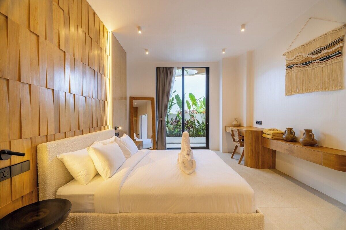 Een hotelkamer met een bed, een bureau, uitzicht op groen en houten wandpanelen.