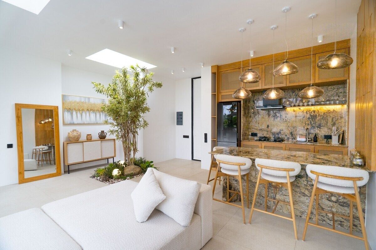 Une cuisine moderne dotée d’un îlot central, de tabourets de bar, de luminaires suspendus et d’une grande plante.
