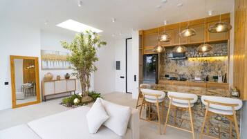 Une cuisine moderne dotée d’un îlot central, de tabourets de bar, de luminaires suspendus et d’une grande plante.