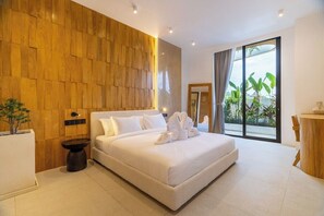 A modern hotel room with a large bed, wooden panel wall, and a view of greenery through the window. - Serene 2BR Villa in Ungasan- Close to Beach + Pool (Badung Regency)