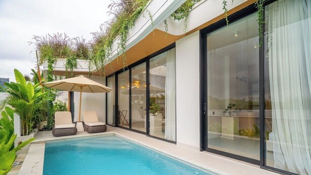 A modern pool area with a glass-enclosed room, outdoor seating, and lush greenery. - Serene 2BR Villa in Ungasan- Close to Beach + Pool (Badung Regency)