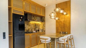 A modern kitchen with a black refrigerator, wooden cabinets, a marble countertop, and a bar area with stools. - Serene 2BR Villa in Ungasan- Close to Beach + Pool (Badung Regency)