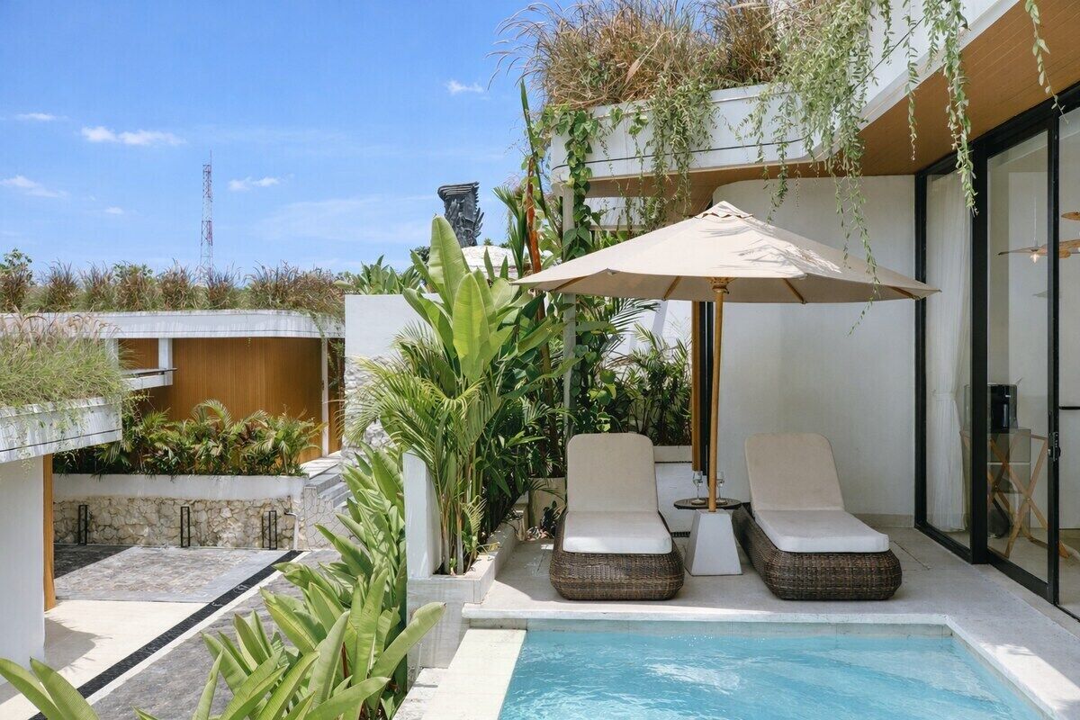 Un espace aménagé au bord de la piscine, avec deux chaises longues, un grand parasol et une vue sur la mer.