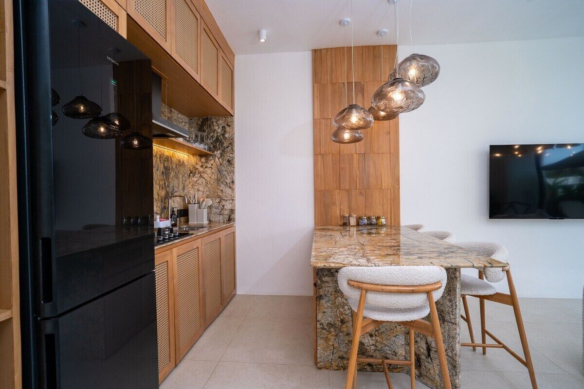 Een moderne keuken met een zwarte koelkast, houten kastjes, een granieten eiland en hangende pendellampen.
